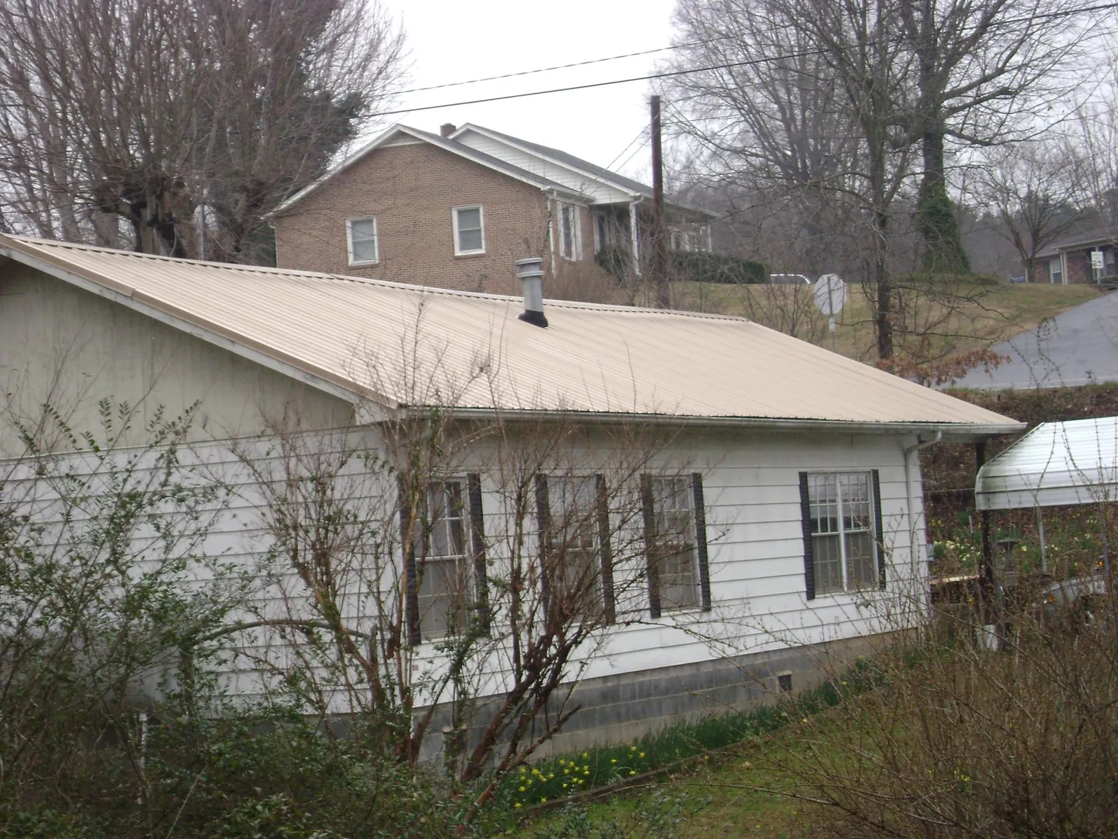 Tan metal roof on a white sided house set into a hillside — Commercial Roofing by Roofing Brothers in Battle Ground
